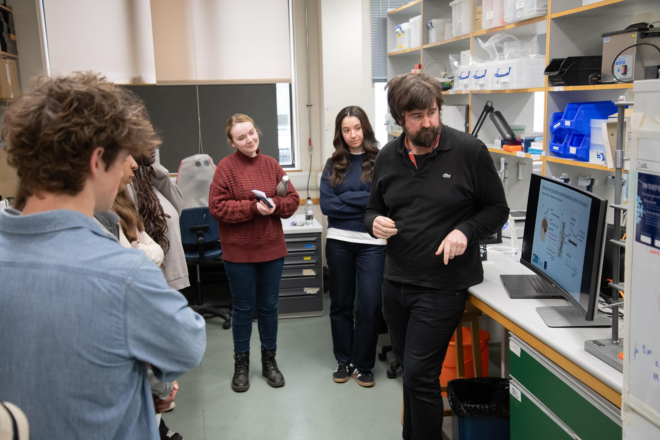 Photo of MRC BNDU researcher Brook Perry talking with visiting pupils in a laboratory